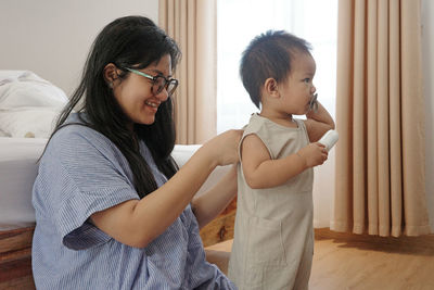 A side view of a young asian mother is dressing her little son. the baby is turned away from his mom