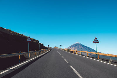 Road leading towards mountain against clear blue sky