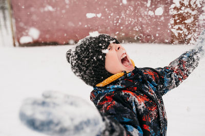 Preschool boy throws snow and is very happy about the winter in warm clothes, hat, yellow snood