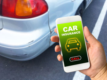 Close-up of hand holding mobile phone by car at street