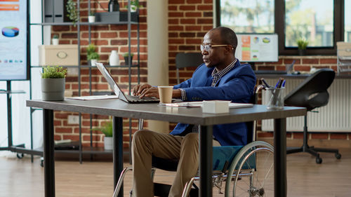 Businessman using laptop sitting on wheelchair in office