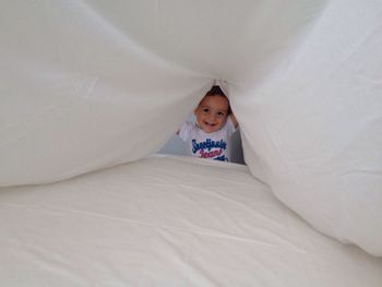 Cute baby boy playing with white bedsheet