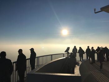 People standing by railing against sky during sunset