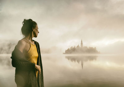 Woman in yellow dress watching a sunrise among the fog on the shores of lake bled, slovenia