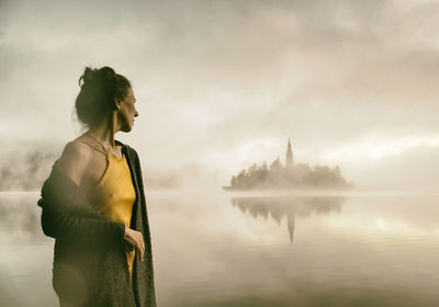 Woman in yellow dress watching a sunrise among the fog on the shores of lake bled, slovenia
