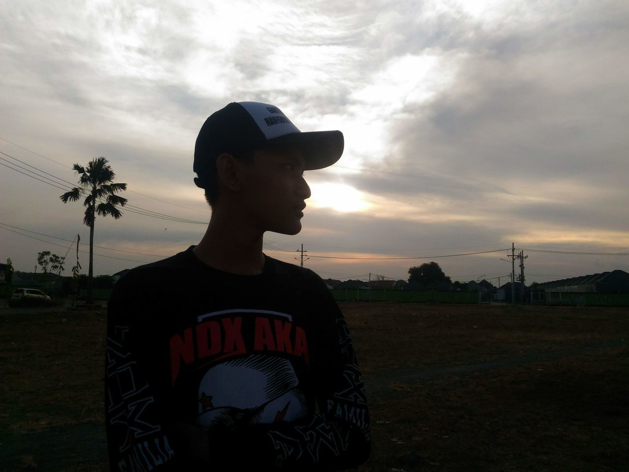 MAN LOOKING AWAY WHILE STANDING ON FIELD AGAINST SKY