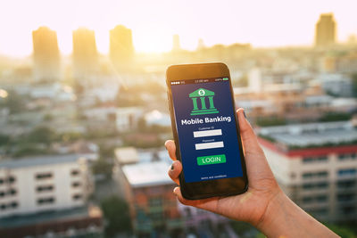 Close-up of hand holding smart phone against cityscape