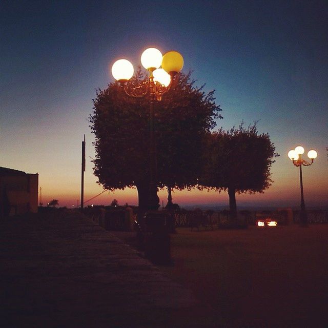 street light, illuminated, tree, sunset, silhouette, lighting equipment, night, sky, clear sky, dusk, tranquility, tranquil scene, nature, orange color, lamp post, outdoors, street, in a row, scenics, road