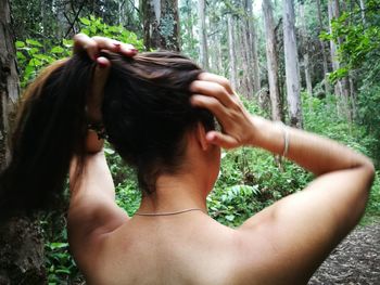 Shirtless woman tying hair at forest