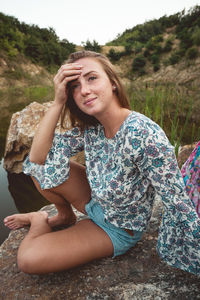 Portrait of a young woman sitting on rock by the lake