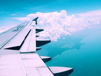 Cropped image of airplane wing over sea against cloudy sky