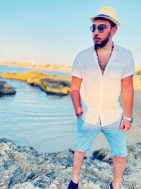 Man wearing sunglasses standing on rock by sea