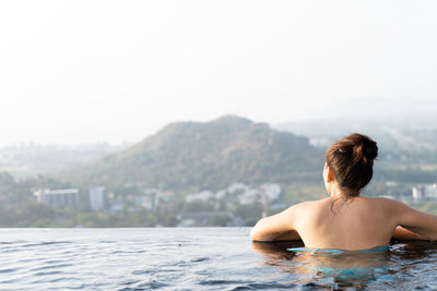 Rear view of woman in infinity pool against clear sky