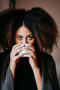 Portrait of young woman with fizzy hair drinking coffee