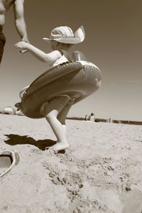 Midsection of father with daughter wearing inflatable at beach against clear sky