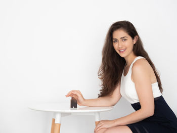 Side view portrait of smiling young woman sitting against white background