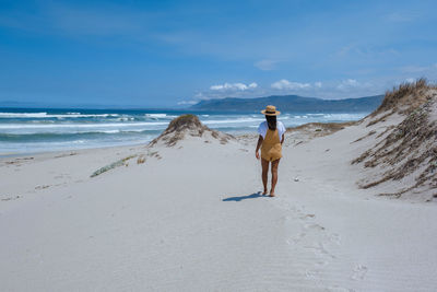 Rear view of woman walking at beach against sky