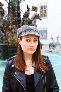 Portrait of beautiful young woman standing against fountain during winter