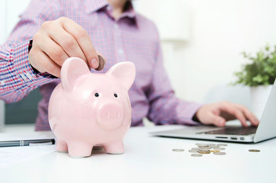 Midsection of businessman putting coin in piggy bank