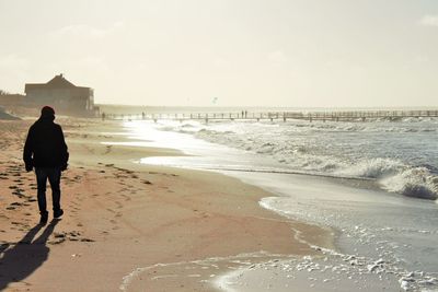 Rear view of man standing on beach against sky