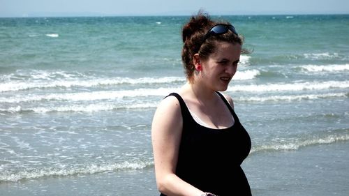 Beautiful woman looking away while standing at beach during sunny day