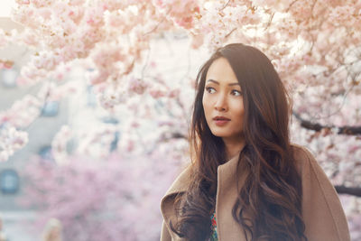 Young asian woman, in front of blossoming cherry tree in the spring time