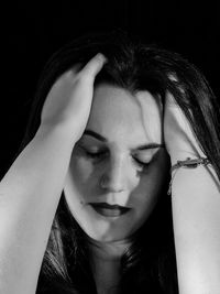 Beautiful young woman with head in hands against black background