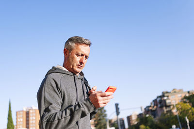 Man using mobile phone against clear blue sky