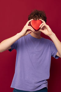 Young man holding heard shape against red background