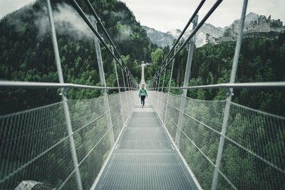 Young female hiking over suspension rope bridge in alpine environment