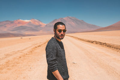 Young man wearing sunglasses standing on desert