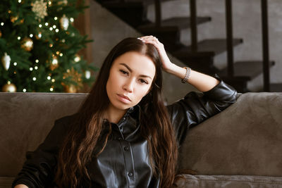 Caucasian happy woman in leather shirt with long sleeves sits on gray sofa