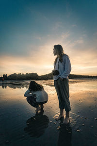 Friends enjoying at beach against sky during sunset