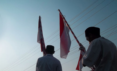 Low angle view of people holding flags while standing against clear sky