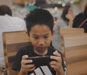 Close-up of boy using mobile phone while sitting on chair