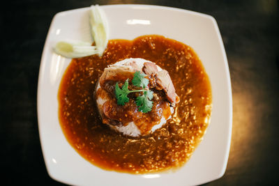 A plate of chinese bbq pork on rice with gravy on top.