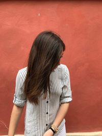 Teenage girl with long hair standing against red wall