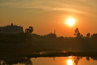 Scenic view of lake by buildings against sky during sunset