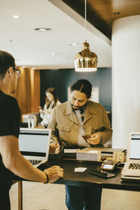 Man looking at tourist signing at reception desk in hotel