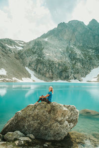 Man on rock by lake against mountains