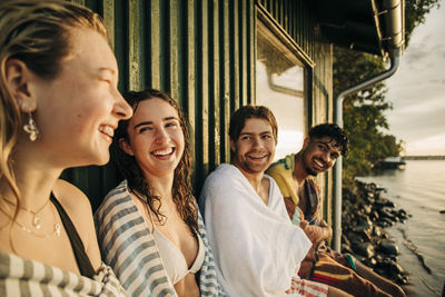 Happy male and female friends with towel sitting by cottage