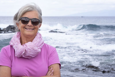 Portrait of senior woman wearing sunglasses standing at beach