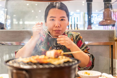 Portrait of woman eating food by barbecue grill in restaurant