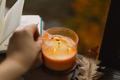 Hand with burning match lighting a candle on the windowsill with autumn decor