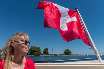 Mature blonde woman with sunglasses smiling and swiss flag fluttering on the stern of a boat
