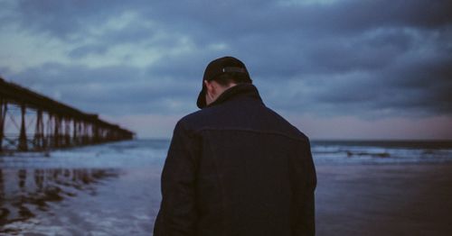 Rear view of man standing at beach during sunset