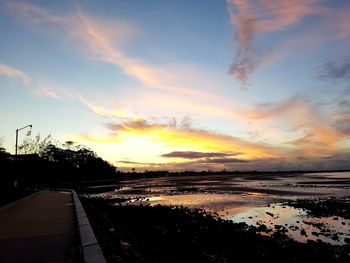 Road by sea against sky during sunset