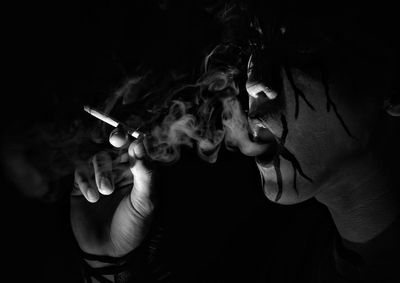 Close-up of man holding cigarette against black background