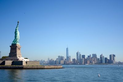 Statue of liberty by cityscape against clear sky