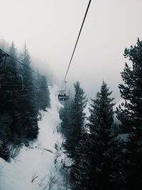 Ski lifts over snow covered landscape during foggy weather